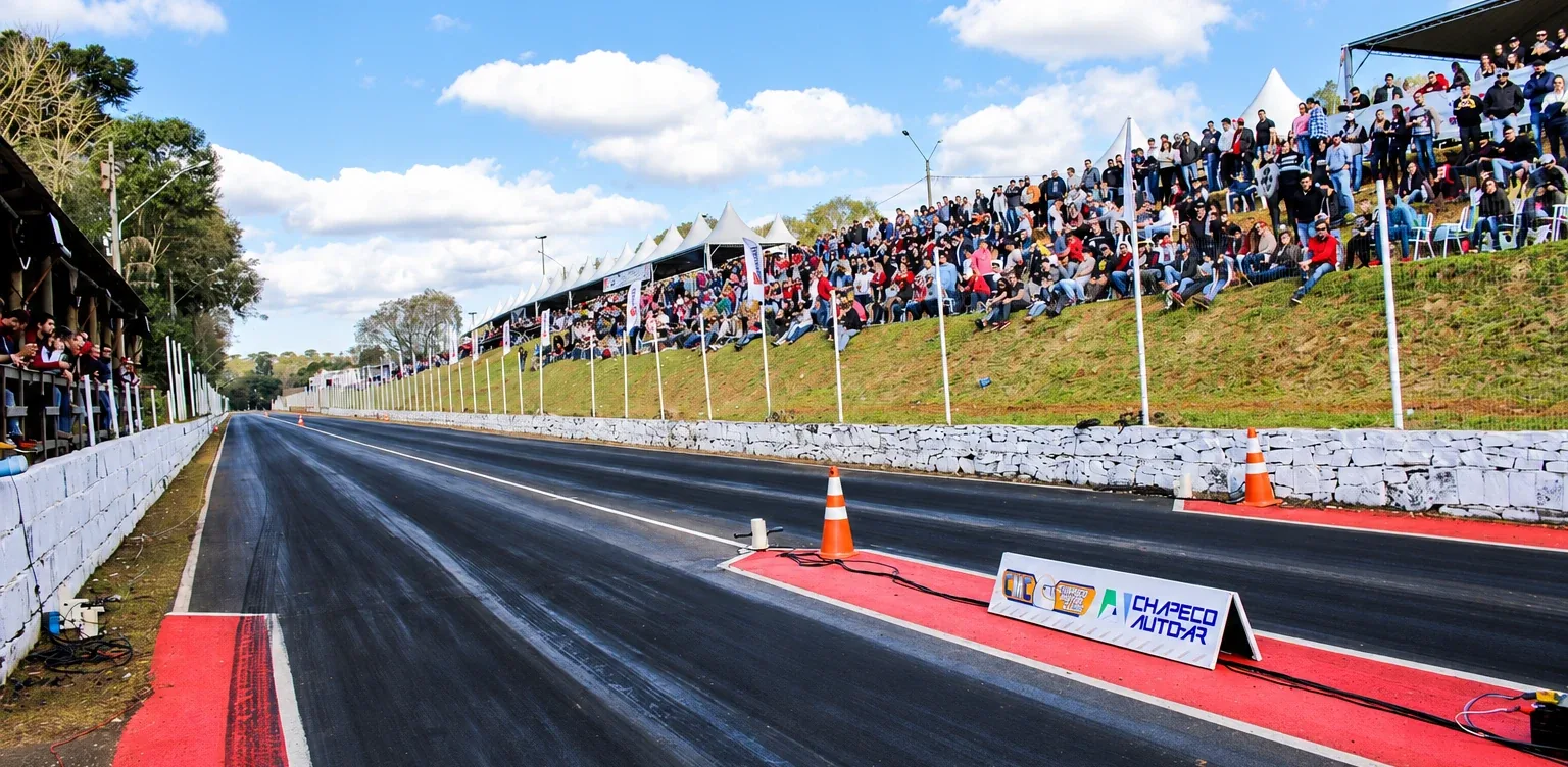 Pista de arrancada com arquibancada lotada e placa da Chapecó Auto-Ar junto à largada